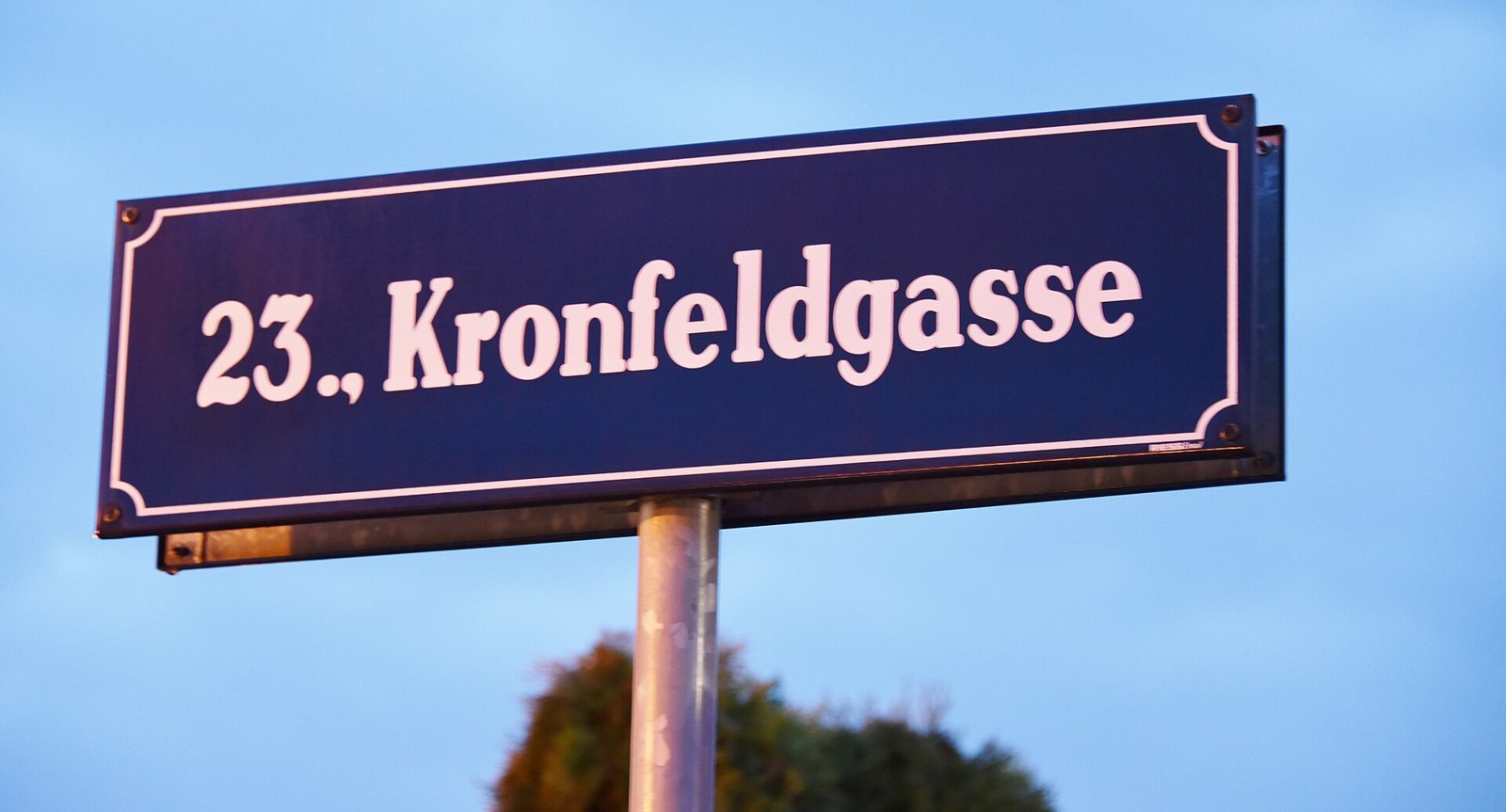 A Viennese enamel street sign reading 23., Kronfeldgasse against a blue sky, the leading number showing the district