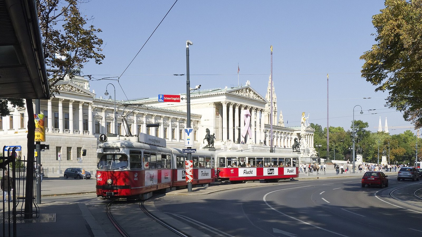 A red Vienna tram passing the Parliament building on the Ringstrasse